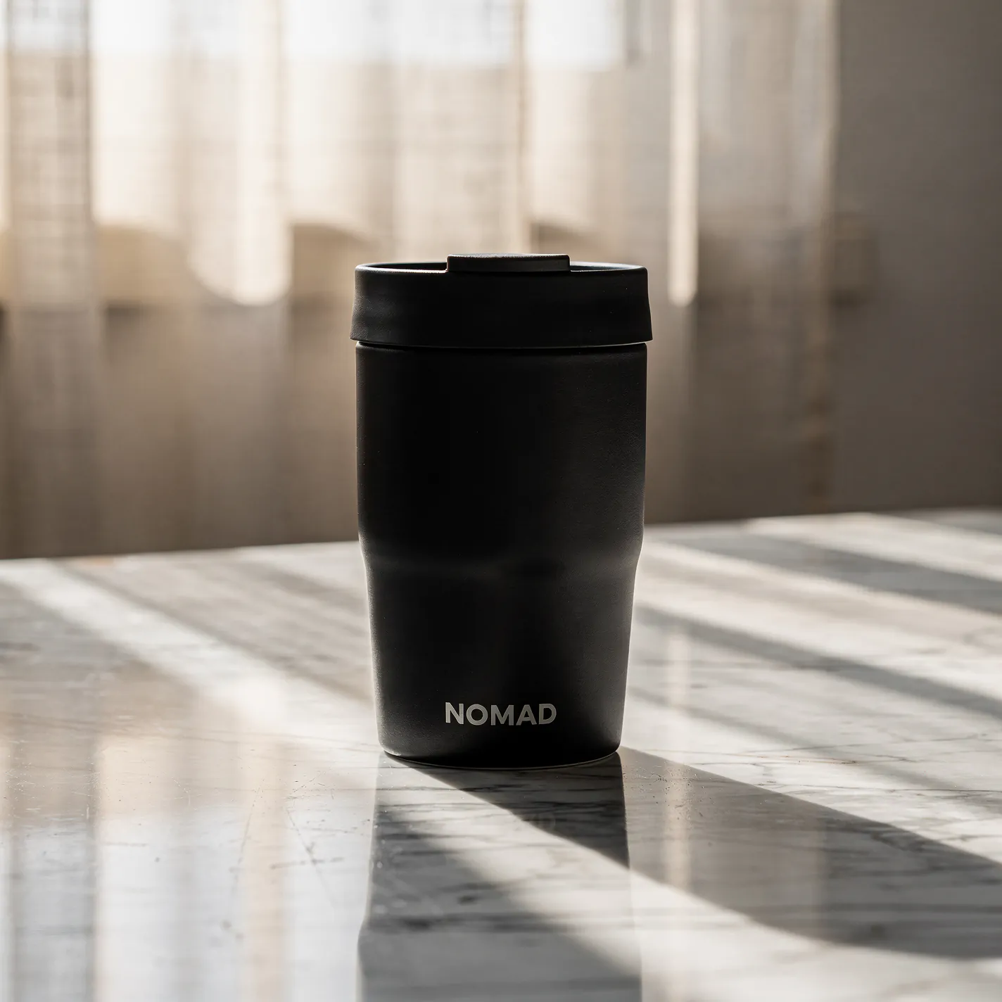 Flux 2 Pro editorial product photo of a matte black NOMAD ceramic travel mug on sunlit marble
