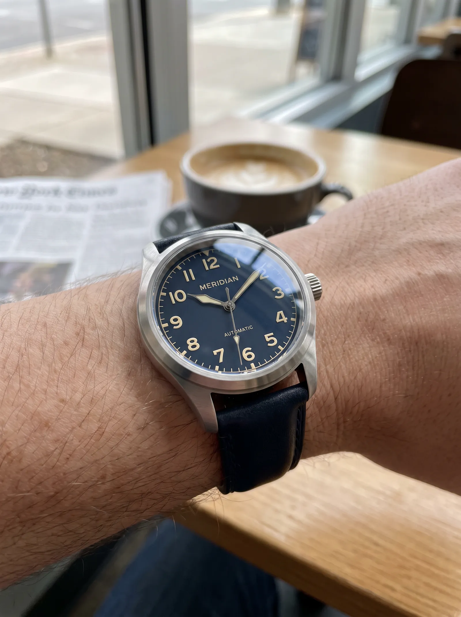 Nano Banana Pro lifestyle wrist shot of the MERIDIAN watch in daytime cafe window light