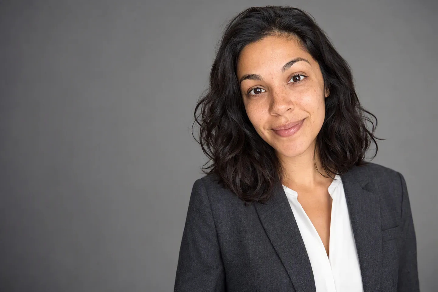 Studio headshot of a woman in a charcoal blazer against a grey backdrop, generated from a selfie